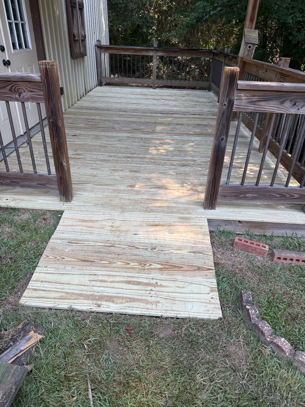 Wooden wheelchair ramp leading to a porch, with railings on both sides and grass below.