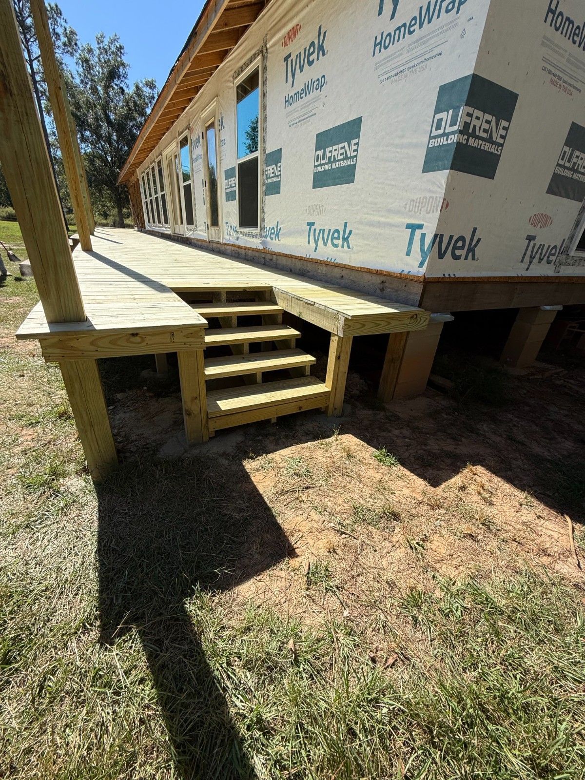 Wooden steps and small deck leading to a Tyvek-wrapped house under construction
