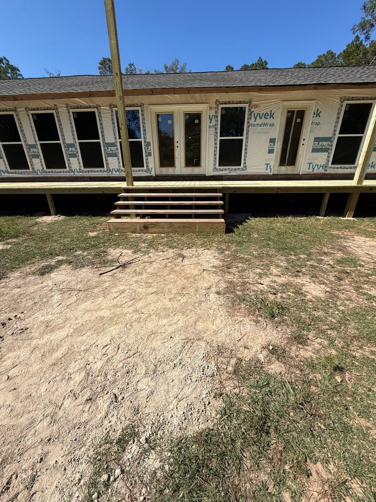 Dilapidated mobile home with front steps and multiple windows on a dirt lot under a clear blue sky