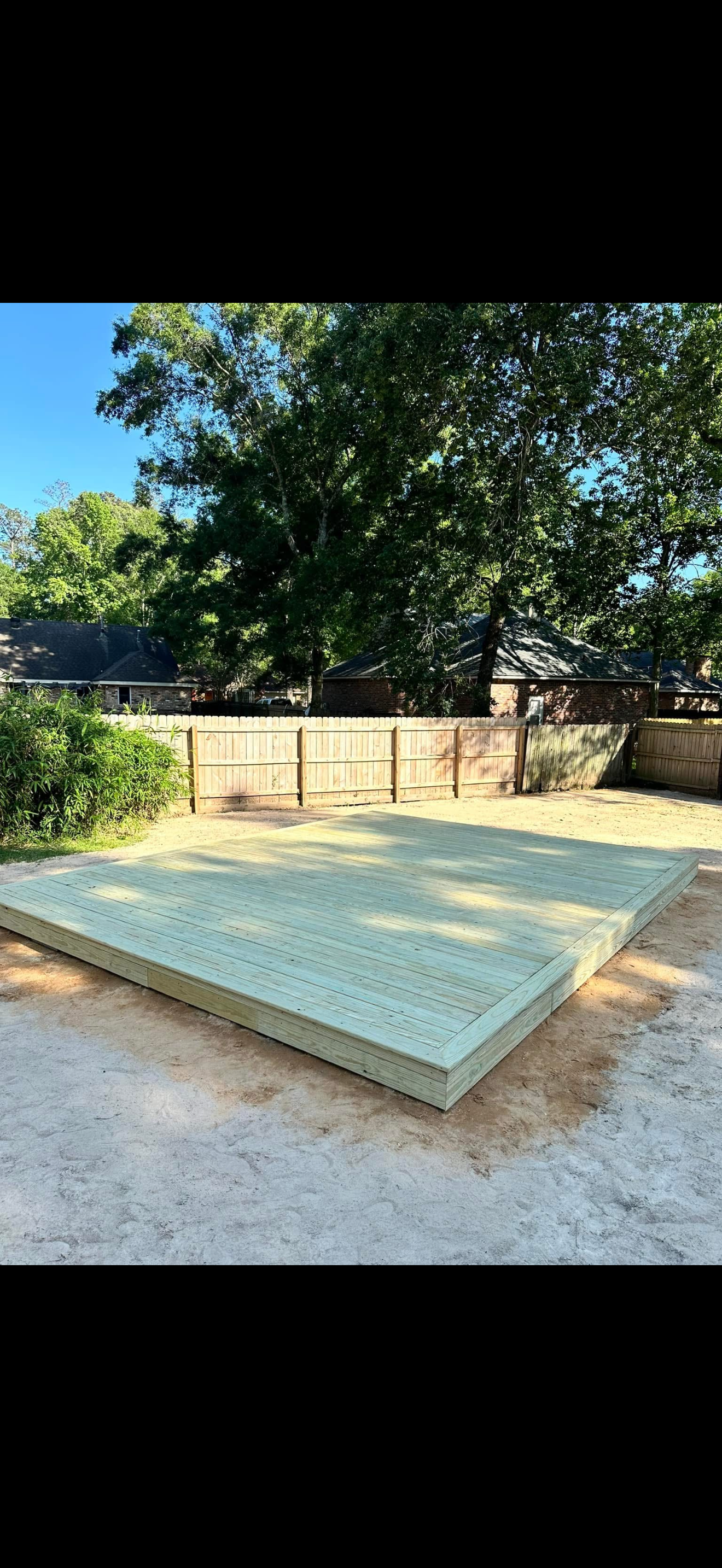 Low concrete platform in a sunny yard with a stone wall and large tree behind it