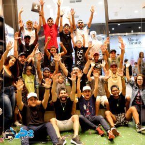 Grupo de pessoas com os braços erguidos, comemorando em um ambiente fechado. Muitas sorrindo, parecendo alegres em uma loja.