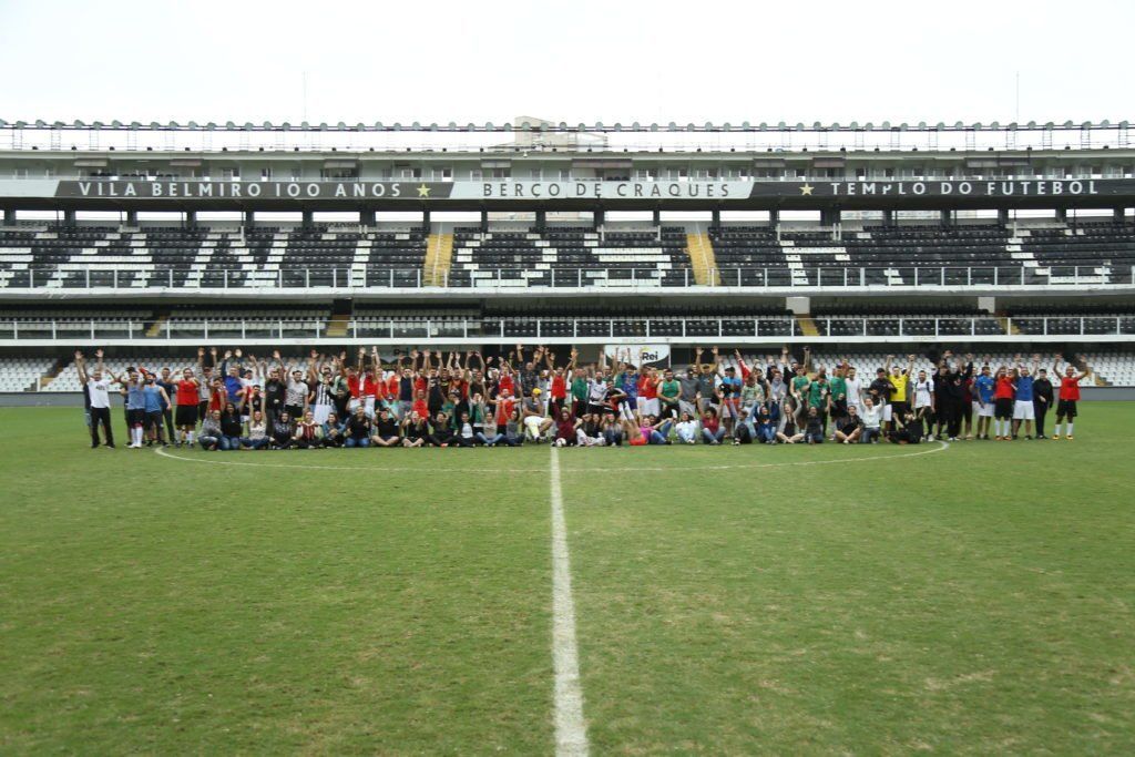 Grande grupo de pessoas em um campo de futebol em frente a um estádio com o 