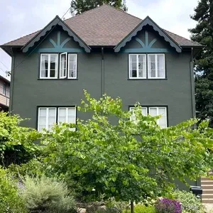 Exterior painting of two-story green house with white window frames, brown roof and green trim. Lush green bushes in front.