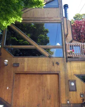 Exterior painting of wood-clad modern house with large windows, wooden door, and a balcony with plants.