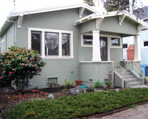 Green bungalow with porch, steps, and landscaping.