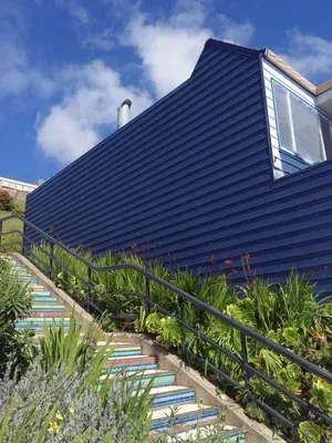 Colorful tiled steps ascend a hillside, flanked by greenery and a navy blue building.