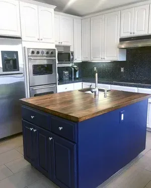 Blue kitchen island with wooden countertop in a white kitchen with stainless steel appliances.
