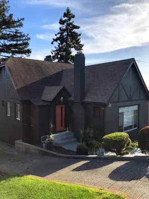 Dark gray house with red door, chimney, and a driveway, under a blue sky.