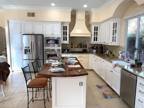 White kitchen with stainless steel appliances, a wooden island, and granite countertops.