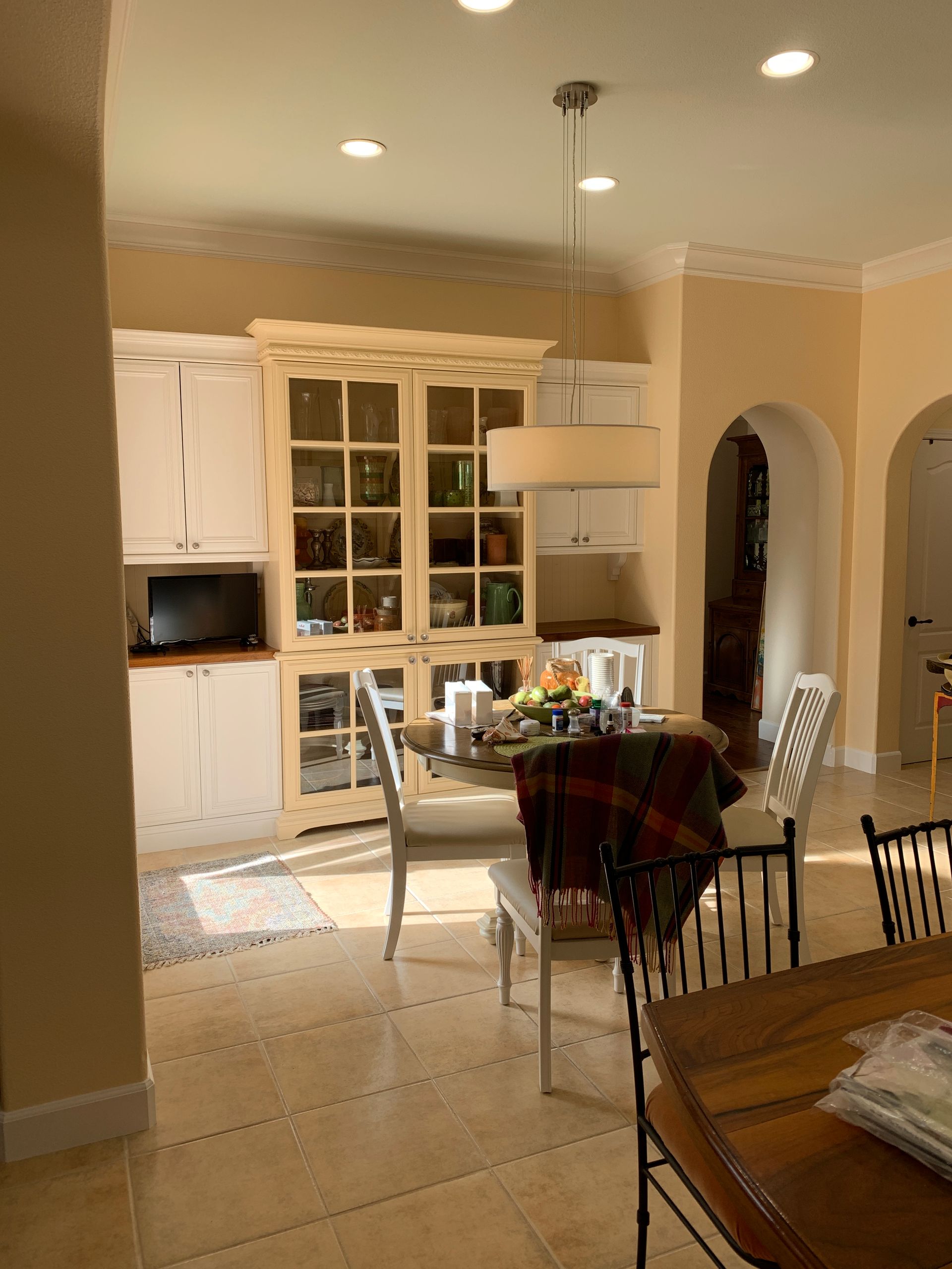 Bright kitchen with white cabinets, dining table, and arched doorway under warm ceiling lights