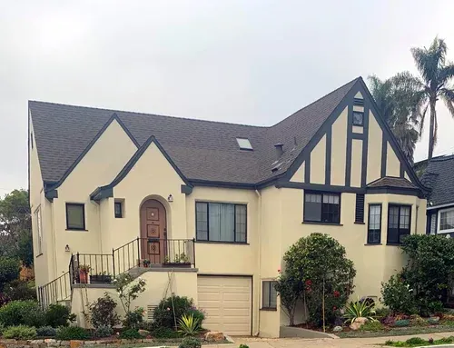 Tan stucco house with dark roof, black trim, and small garden.