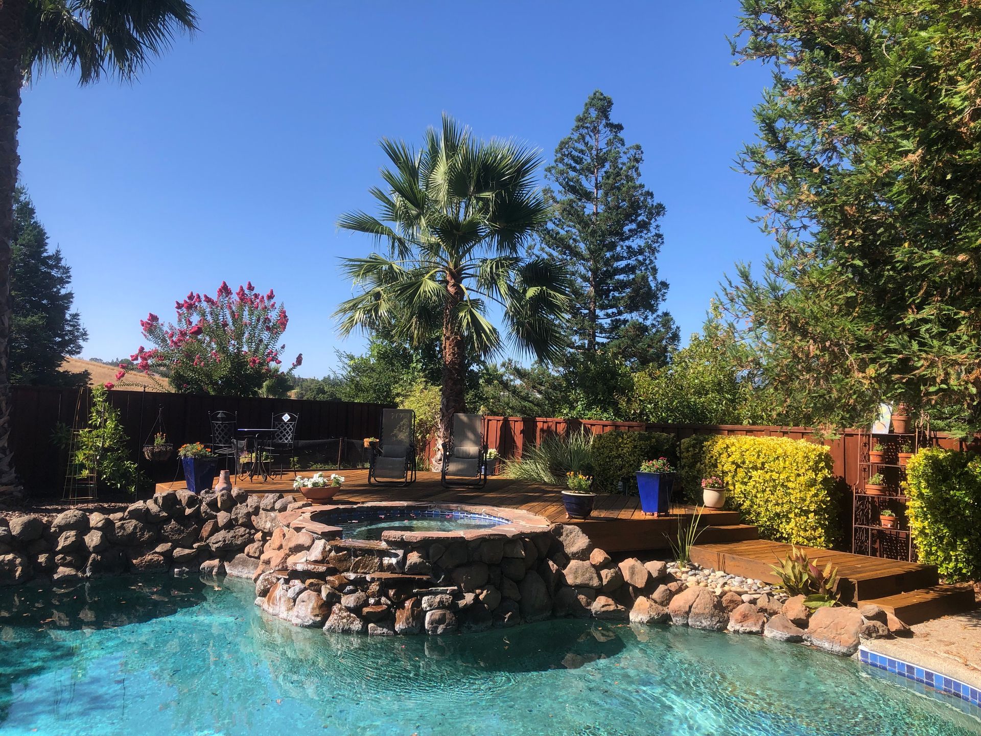 Backyard pool with rock waterfall, palm trees, and bright blue water under a clear sky