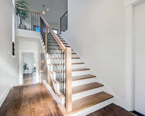 Wooden staircase with metal railings in a home's entryway, leading to an upper level.