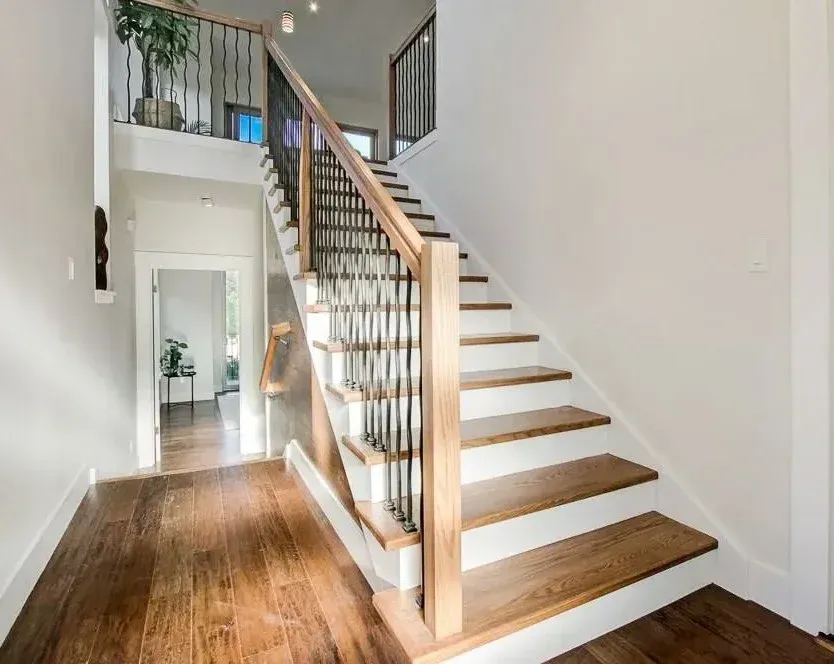 Interior painting of home with wooden staircase with white risers, brown treads, and black iron railing.