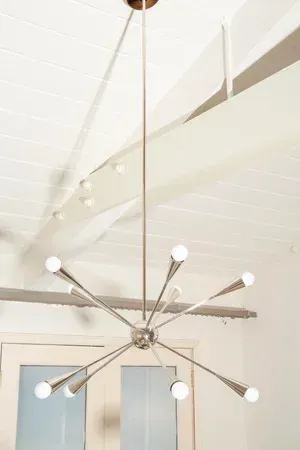 Silver starburst chandelier hanging from a white ceiling with exposed beams.