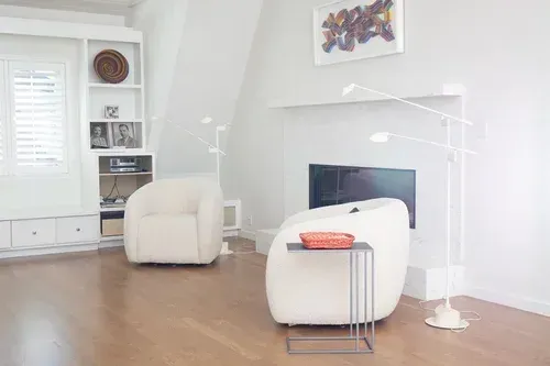 Bright, modern living room with white chairs, fireplace, and hardwood floors.