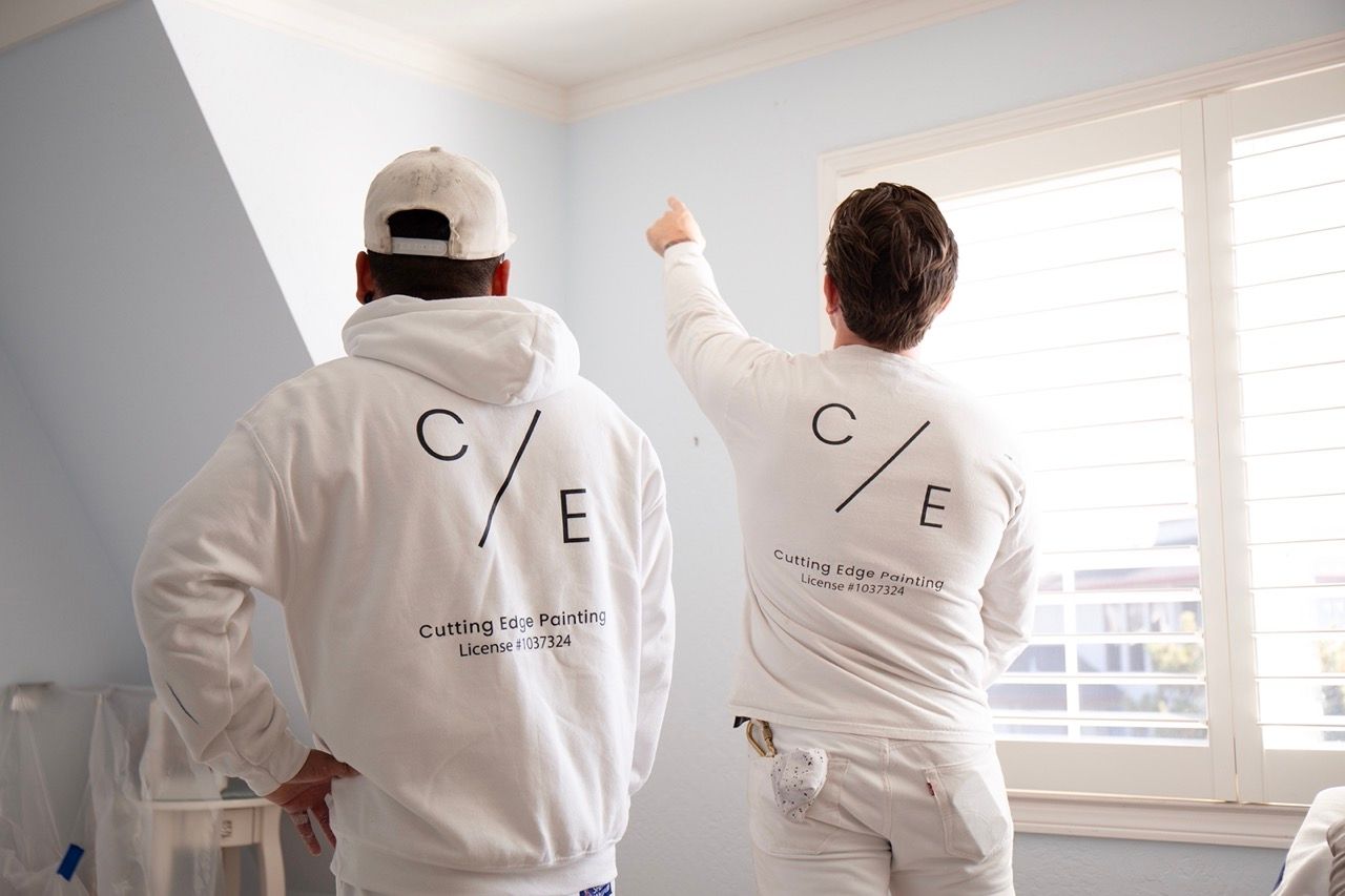 Team of Cutting Edge Painters workers in white hoodies paint a bright room near a window