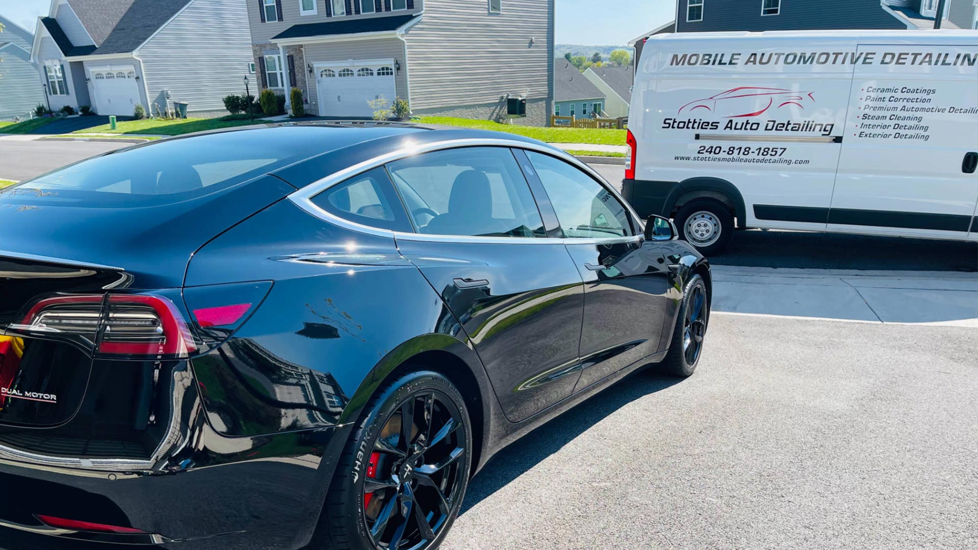 a black tesla model 3 is parked in a driveway next to a white van .