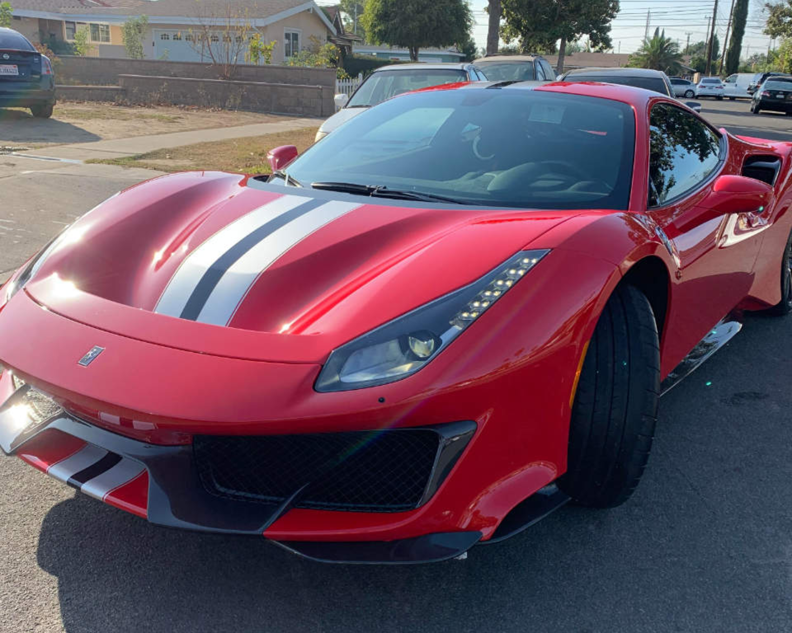 Red Ferrari sports car with white racing stripes parked on a residential street.