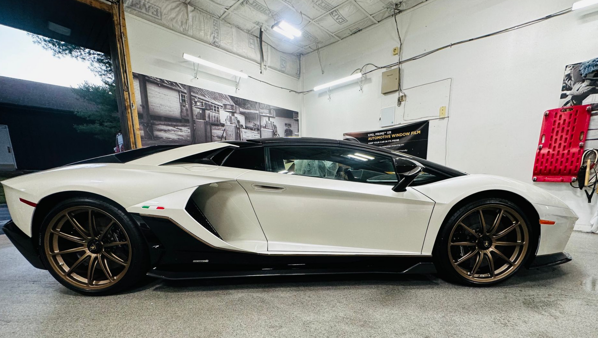 White and black Lamborghini Aventador inside a garage. Bronze wheels, black roof, and accents.