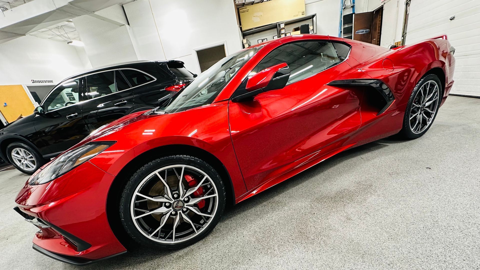 A red sports car is parked in a garage next to a black car.