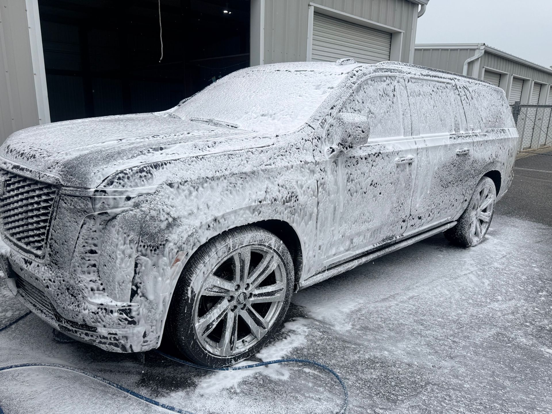 SUV covered in white foam, undergoing a car wash outside a building.