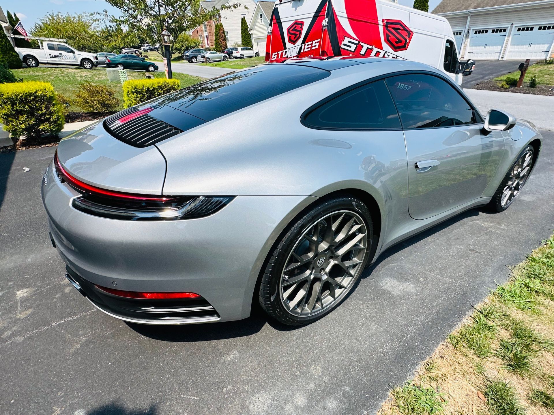 Silver Porsche 911 parked on a paved driveway with a tinted glass roof and windows.