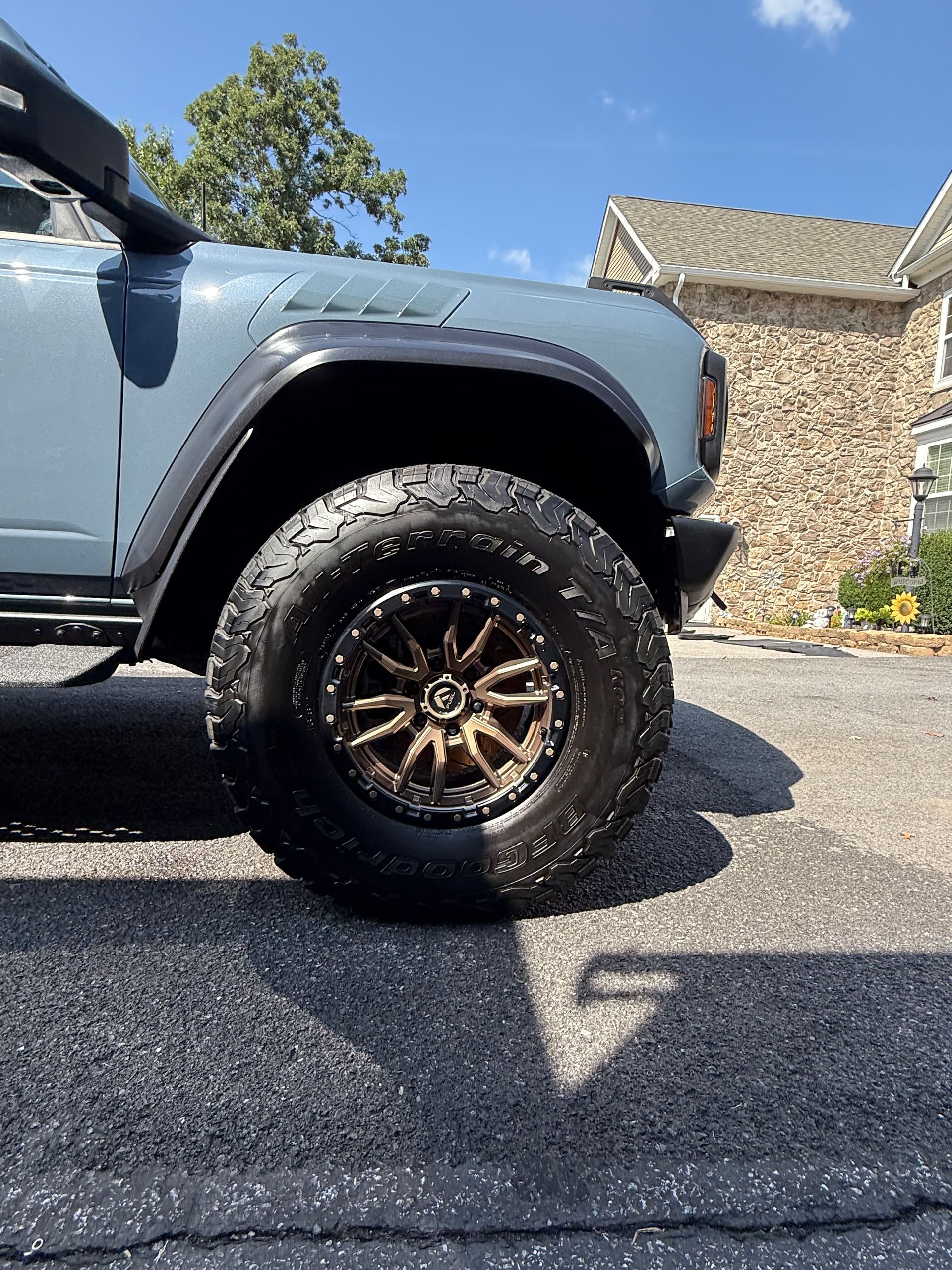 Blue SUV with bronze wheels, parked on asphalt. Sunny day.