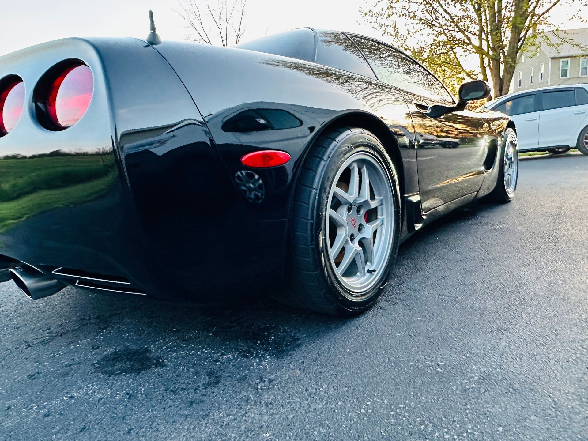 Black Corvette sports car parked on asphalt, rear view, silver rims.