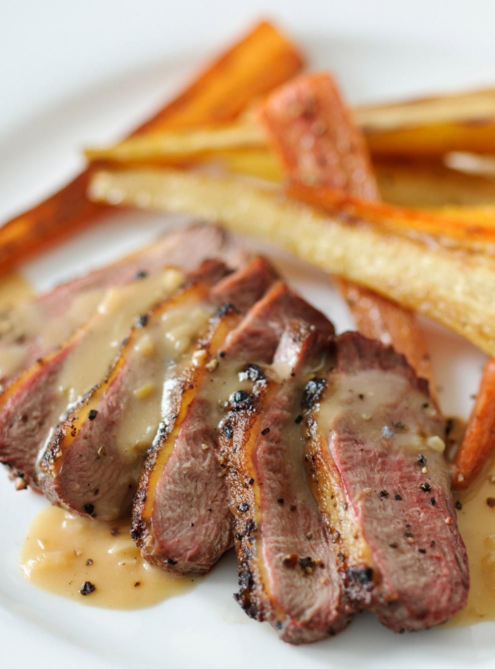 Sliced roast meat with gravy, served with roasted potatoes and carrots on a white plate