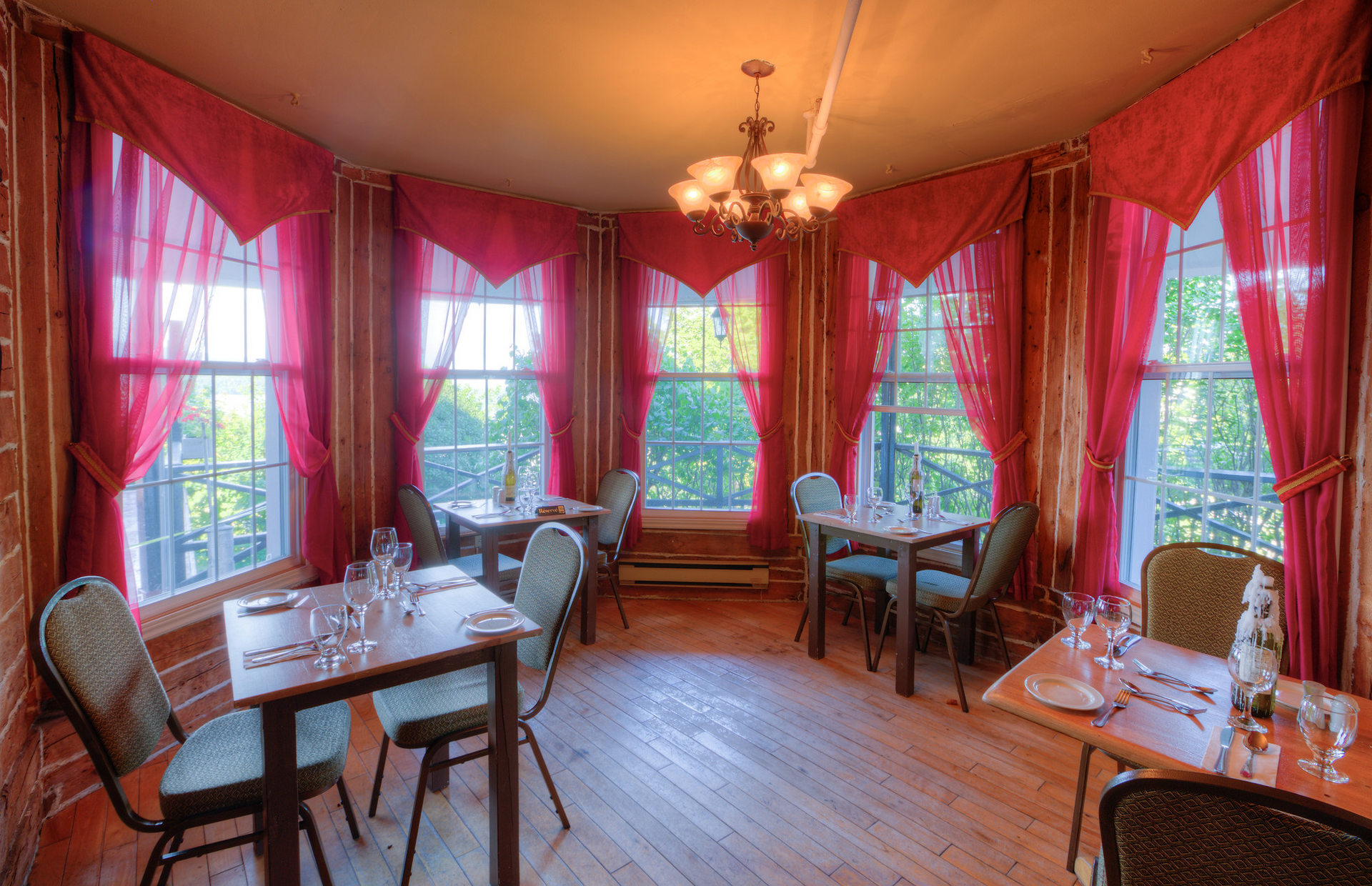 Cozy dining room with pink walls, red drapes, large windows, and wooden tables and chairs