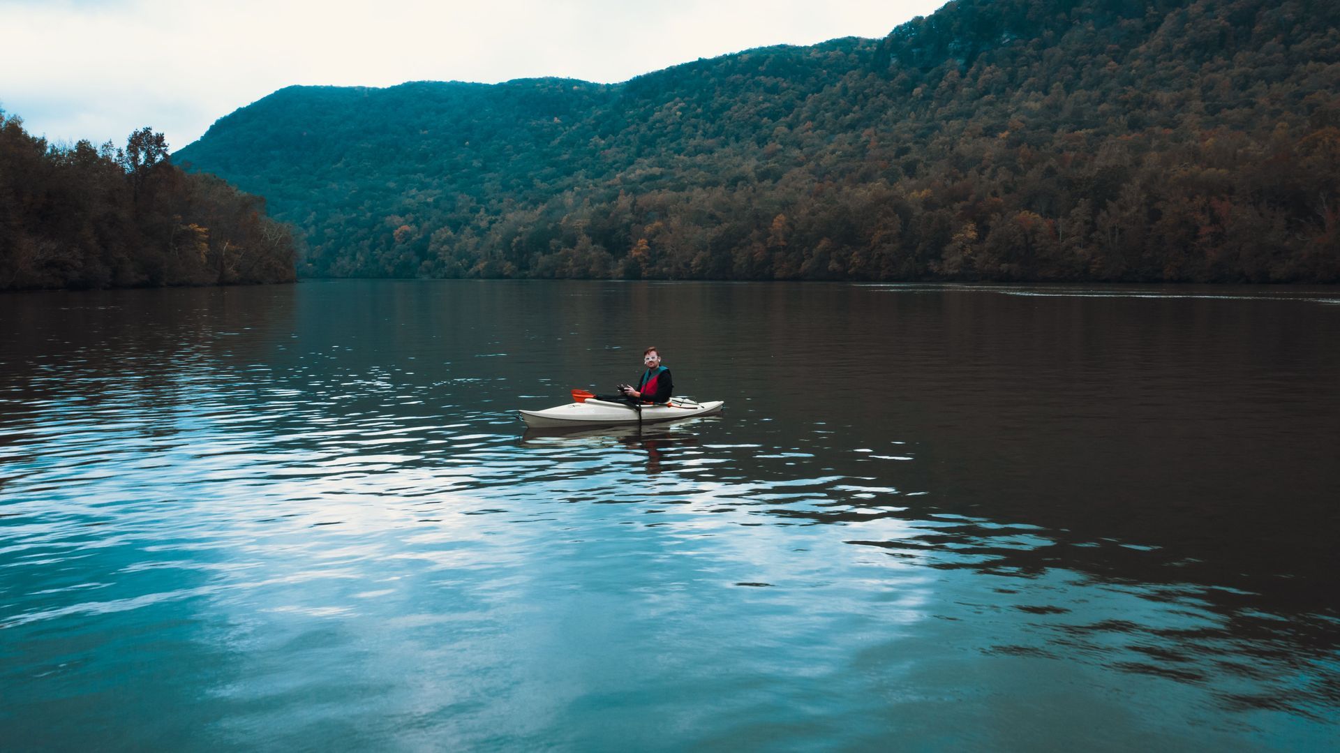 A lone kayaker on a calm lake with forested mountains reflected in the water