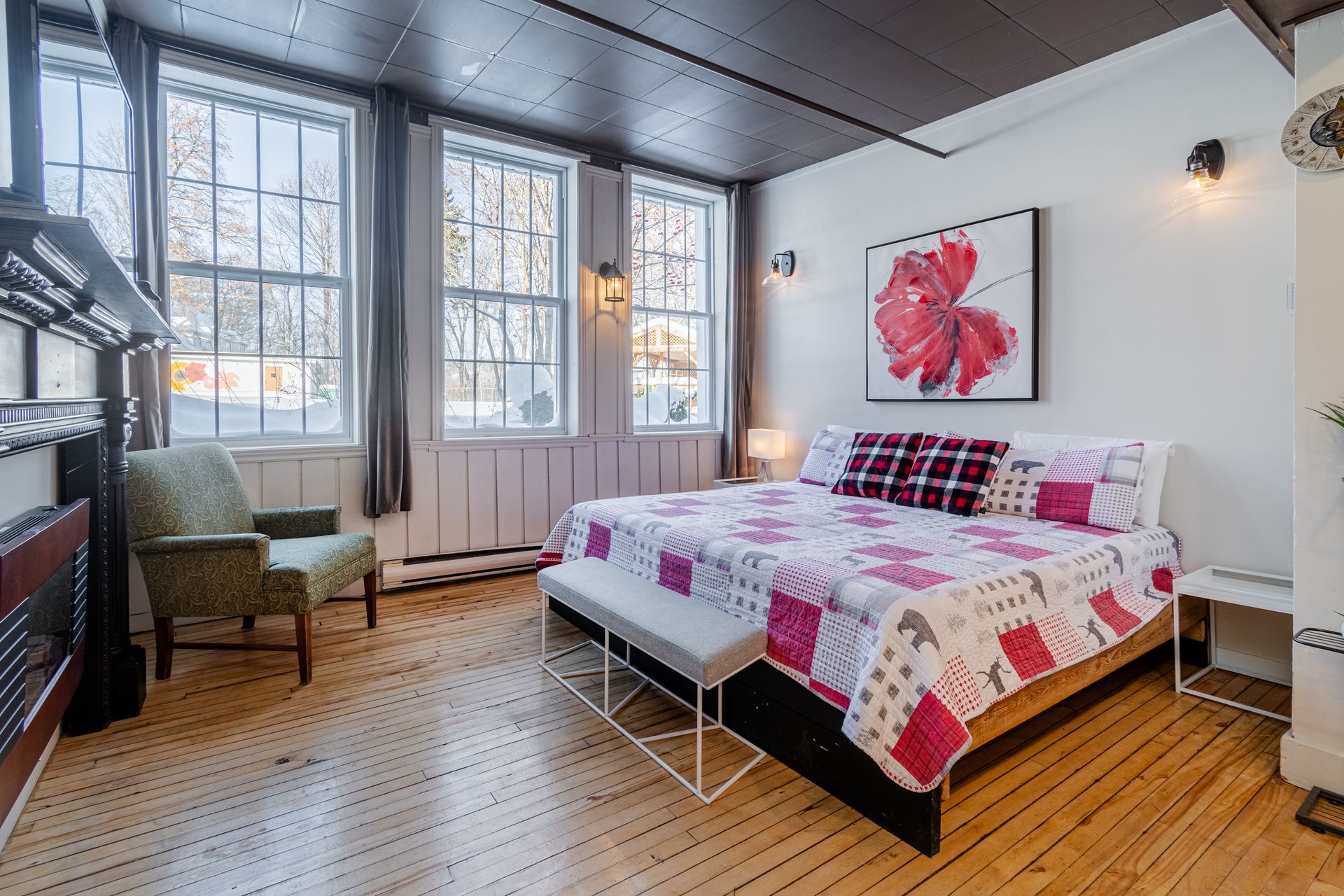Bright bedroom with a bed, red floral art, large windows, and wooden floors
