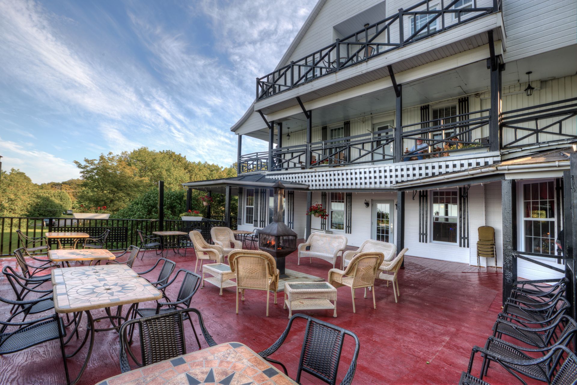 Outdoor patio with wicker tables and chairs beside a white multi-story building with balconies