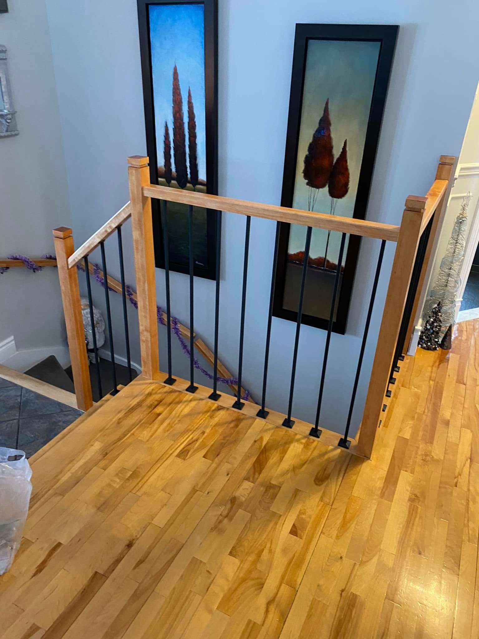 Un escalier en bois avec une rampe en métal et des tableaux au mur.