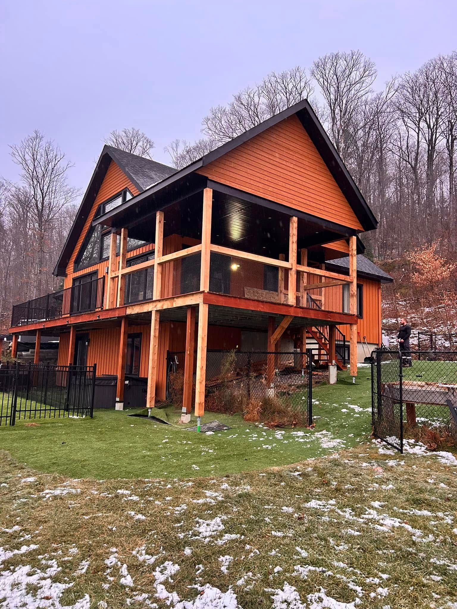 Une grande maison en bois avec une grande terrasse est située au sommet d'un champ verdoyant.