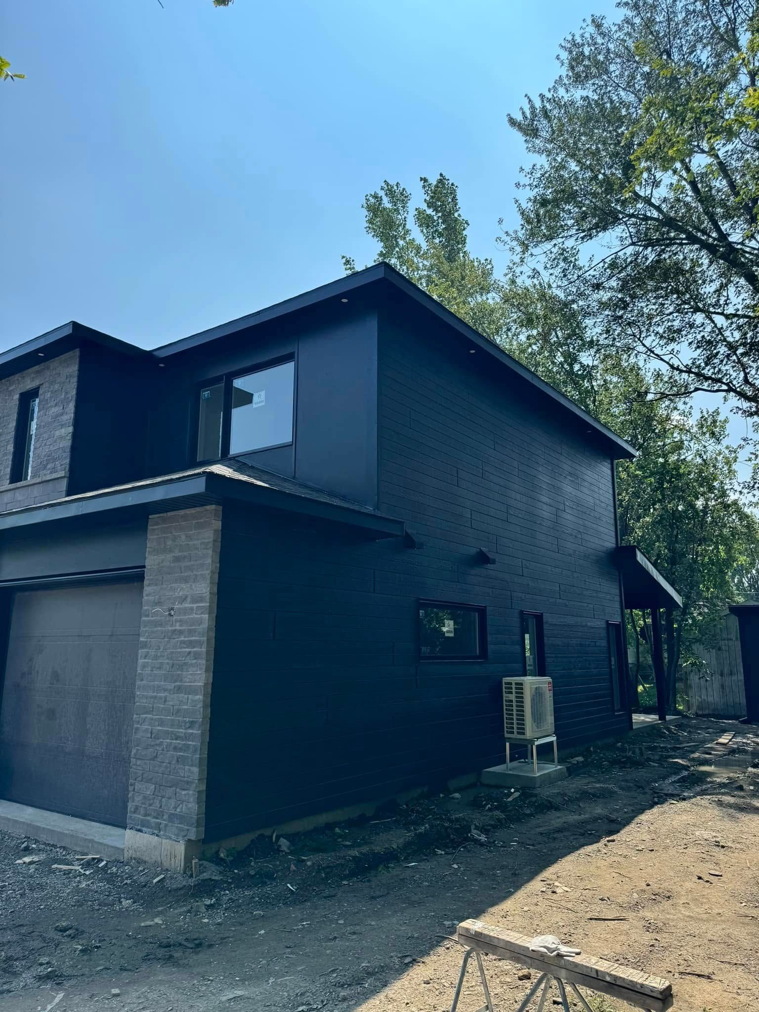 Une maison noire est en train d'être construite au milieu d'un champ de terre.