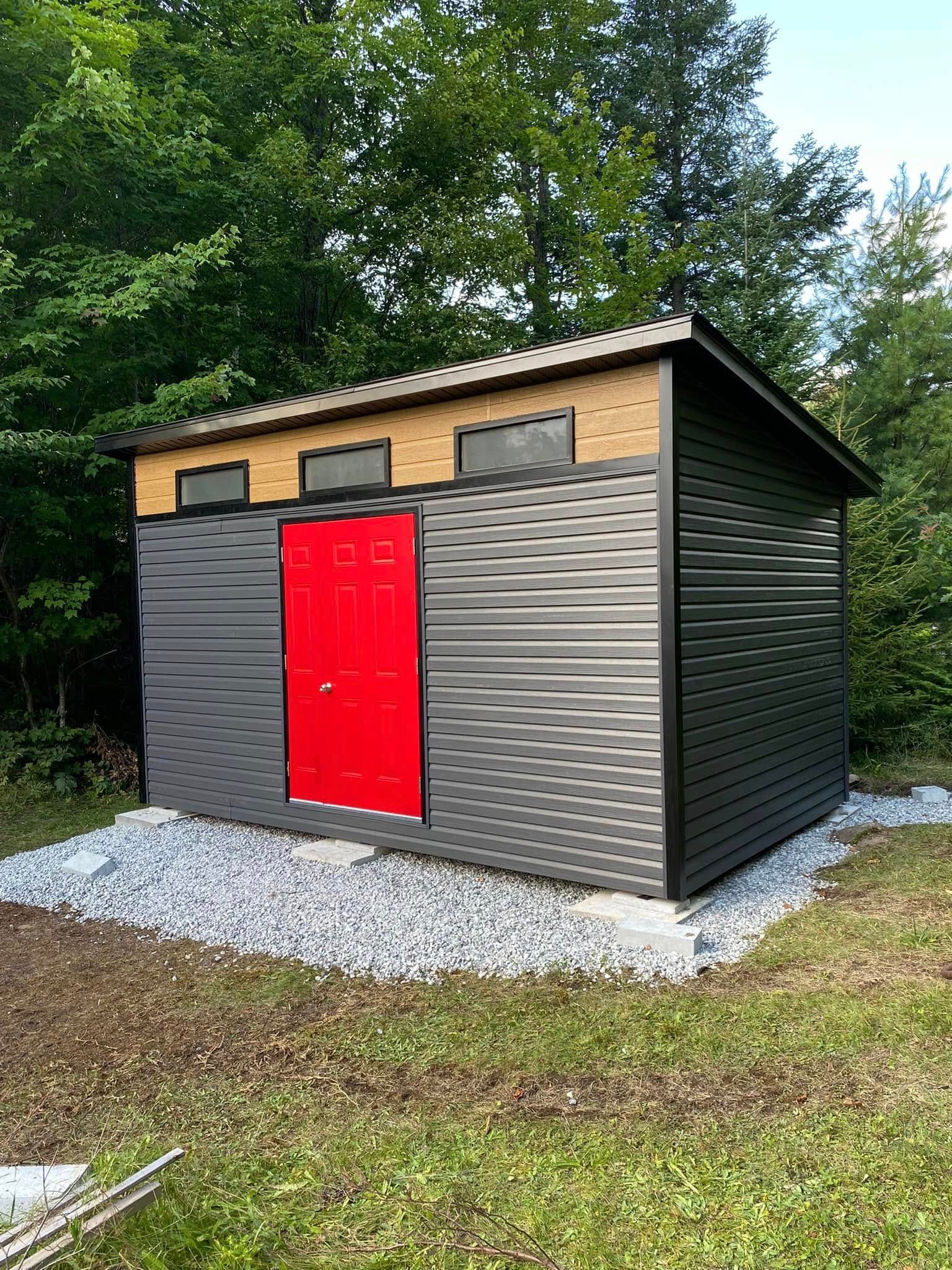 Un hangar avec une porte rouge se trouve au milieu d'un champ herbeux.