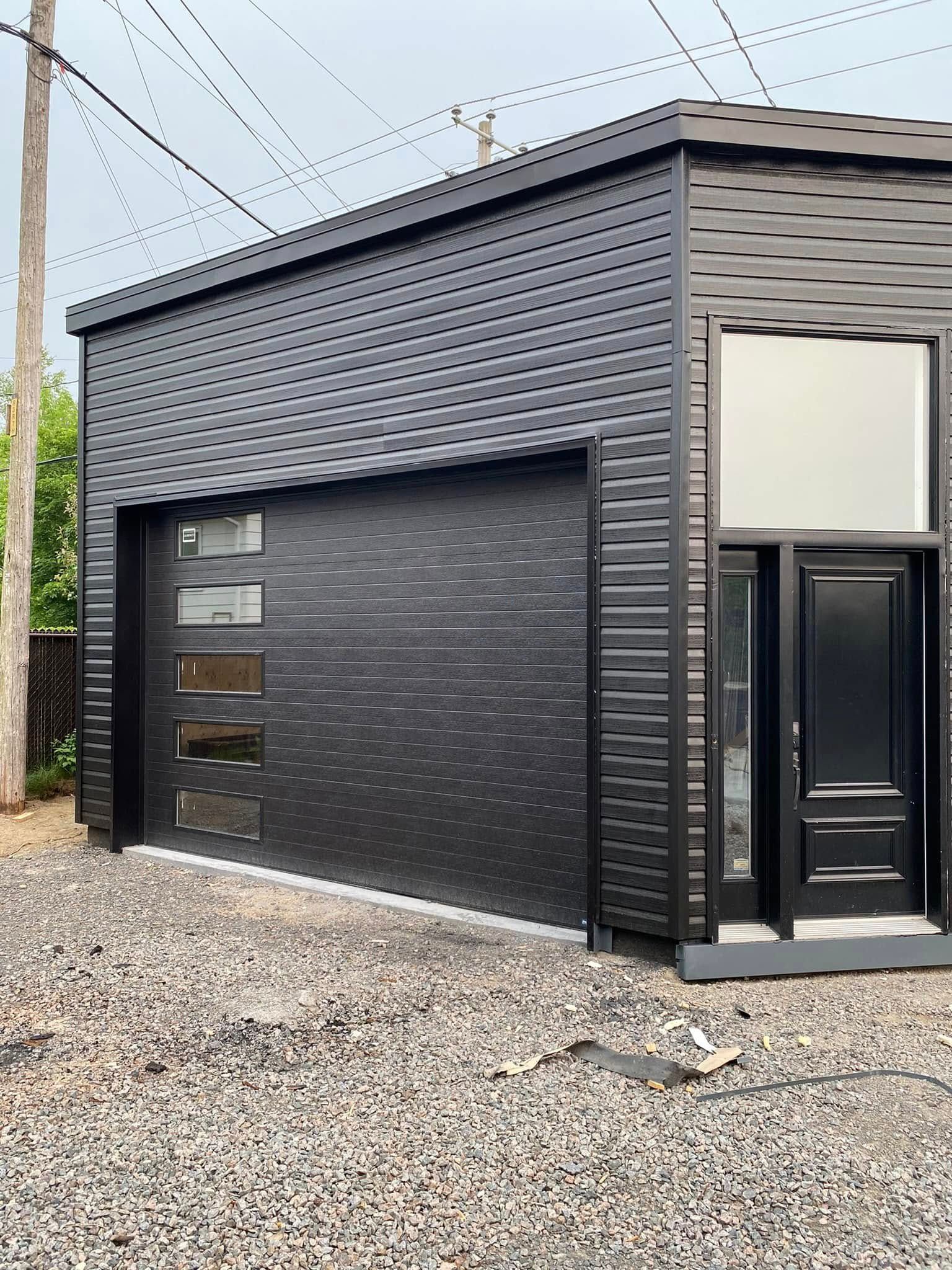 Garage et entrée modernes noirs avec revêtement texturé sur un terrain en gravier.