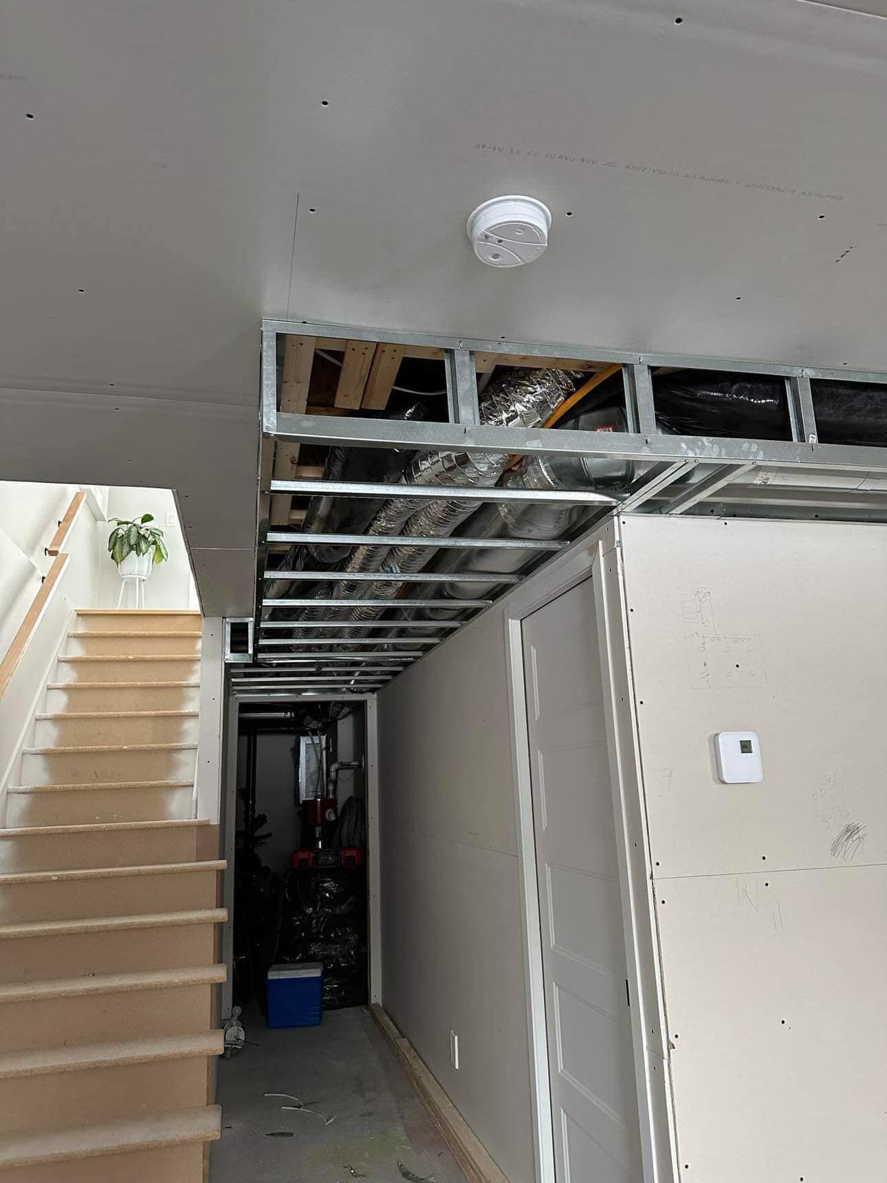 Un couloir avec des escaliers et une alarme incendie au plafond.