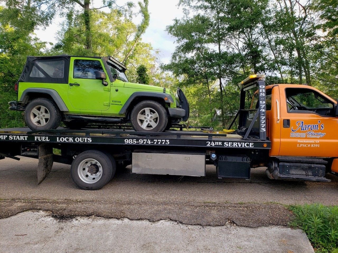 A picture of a tow truck with a green jeep on the back of it with trees in the background in Hammond, LA