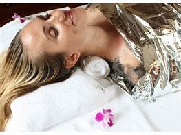 Woman lying on a spa bed with a body wrap applied, covered in towels, enjoying a relaxing treatment.