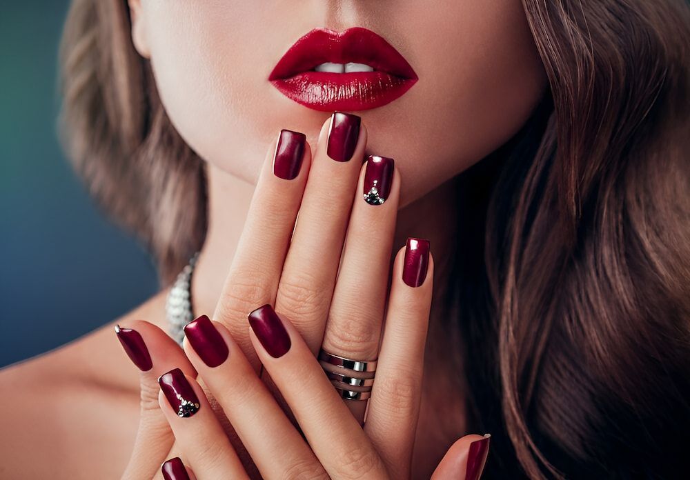 A Woman With Red Lips And Red Nails Is Covering Her Mouth With Her Hands — Bundy Nail & Spa in Avoca, QLD