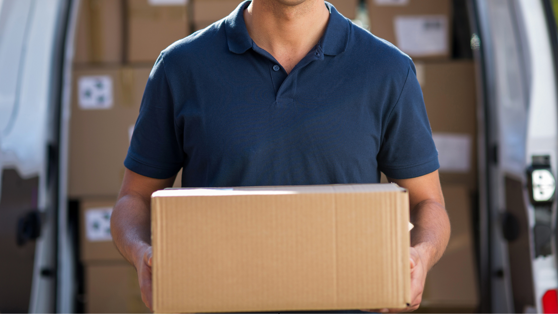 A delivery man is holding a cardboard box in front of a van filled with boxes.