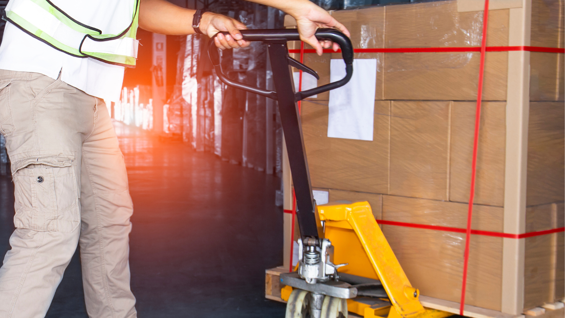 A man is pushing a pallet truck with boxes on it in a warehouse.