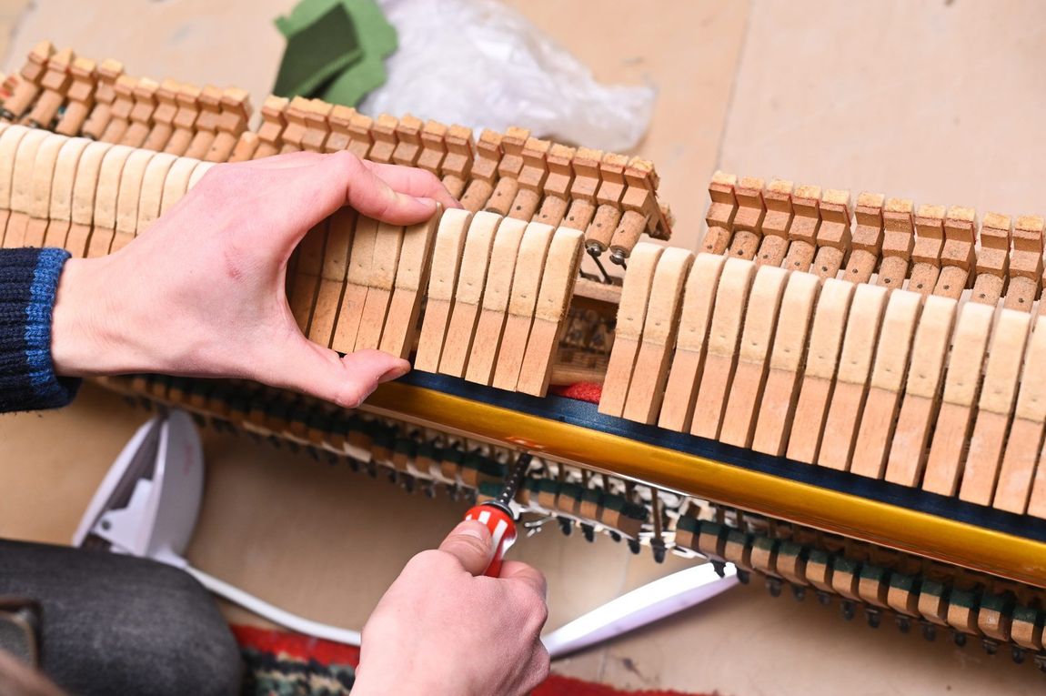 A person is working on a piano with a screwdriver.