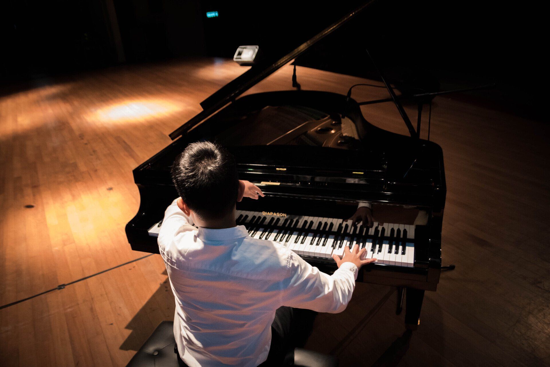 A man is playing a piano on a stage in a dark room.