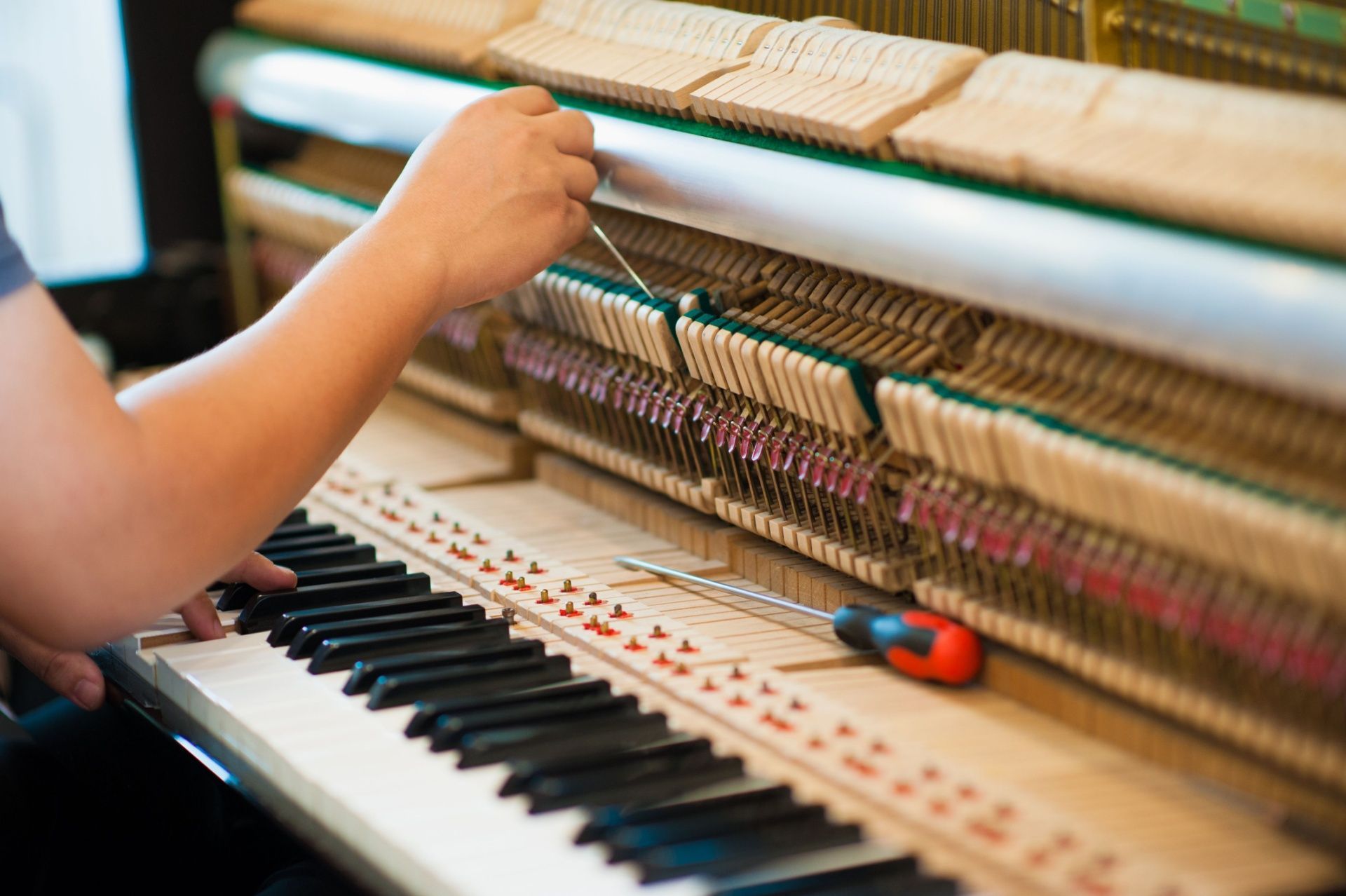 Person tuning a piano with tools, focusing on the inner mechanics of the instrument.