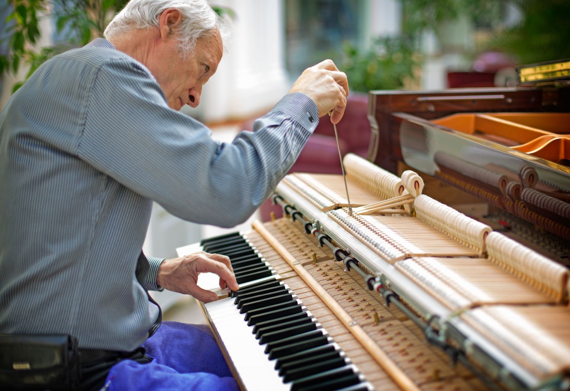 Man tuning a piano. He adjusts strings inside, near the keyboard.