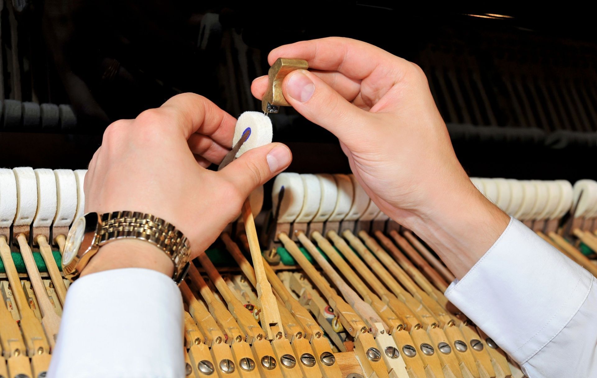 Hands adjusting a piano hammer with a tool inside the piano.